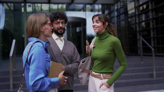 Three diverse coworkers having a friendly conversation in front of a contemporary office entrance having a corporate meeting. 