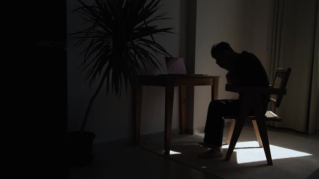 Depressed man sitting at a home workspace after professional setback symbolizing unemployment career uncertainty financial pressure and difficulties in the modern job market