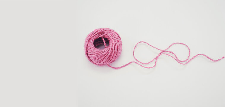Una matassa di spago di colore rosa in primo piano su una superficie bianca e vuota con spazio per testo
