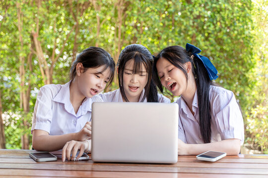 Three Thai high school girls in school uniform sit together and using laptop doing homework on a table. Be diligent and determined. Ready for the final exam