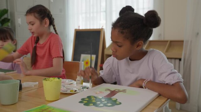 Girl Painting Colorful Artwork at Classroom Table with Brush and Palette, Creating Tree Nature VDO While Classmate Children Explore Creative Learning, Focused Educational Art Session