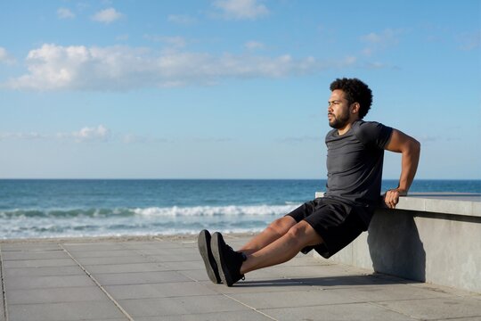 Man performing tricep dips on bench near ocean during outdoor calisthenics workout. Bodyweight fitness and strength training concept