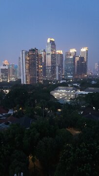 Aerial drone view of Jakarta's Sudirman business district at night featuring illuminated skyscrapers, glowing office buildings, vibrant city lights, and heavy traffic after office hours, showcasing th