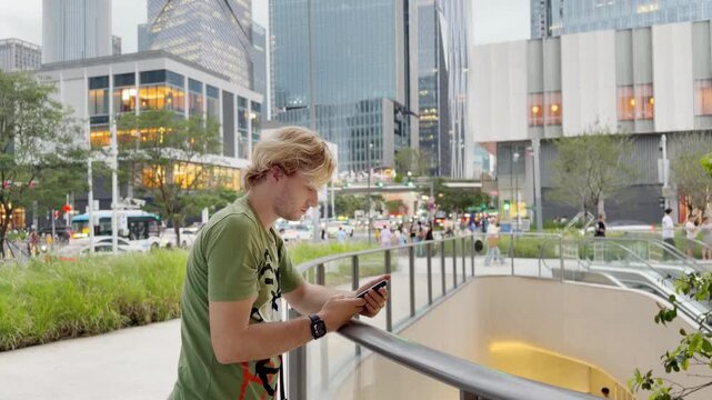 Young Man Using Smartphone Against Skyscrapers &ndash; Talking, Scrolling or Recording Video