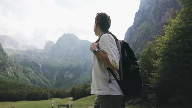 Young female traveler with a backpack enjoying a breathtaking mountain view while standing in a scenic meadow, capturing freedom, adventure and connection with nature.