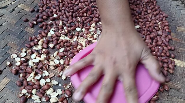 Close Up of Hand Peeling Roasted Peanuts Skin Using Plastic Lid on Traditional Woven Tray