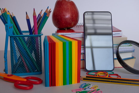School and office desk featuring colorful stationery, books, a red apple, and a smartphone, highlighting modern education, back to school, creativity, and hybrid learning concepts
