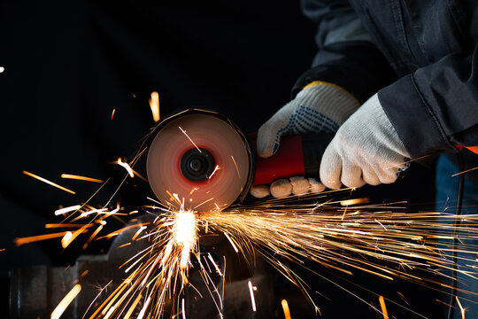 A worker uses an angle grinder to cut metal clamped in a heavy bench vice