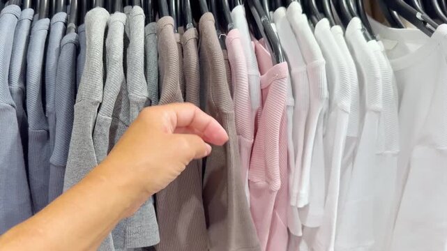 Assorted Casual Clothes on Store Racks.Hand Choosing Clothes on Hangers in Clothing Boutique &ndash; Casual Wear Selection