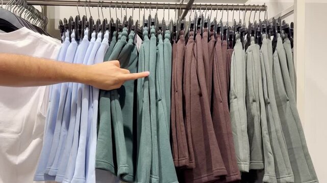 Assorted Casual Clothes on Store Racks.Hand Choosing Clothes on Hangers in Clothing Boutique &ndash; Casual Wear Selection