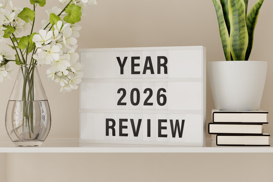 A lightbox displaying the words "Year 2026 Review" on a shelf with books and plants.