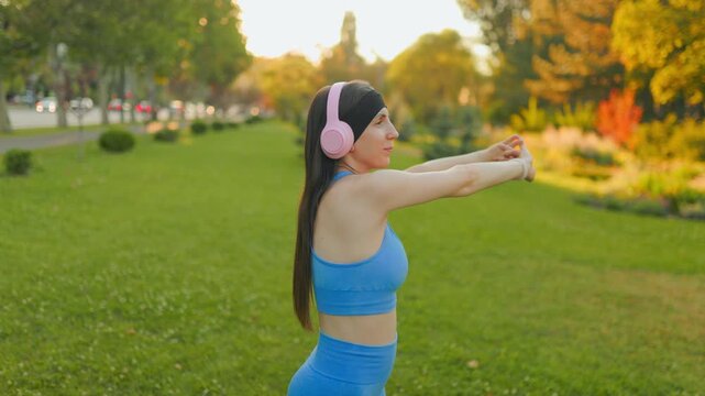 Young female runner stretching arms before fitness workout in the park.