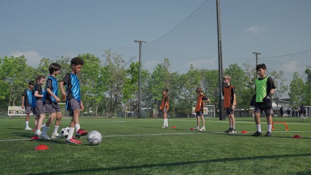 Youth soccer training with child players practicing ball control, dribbling, passing, and teamwork around cones and goals on outdoor artificial turf during active sports practice session