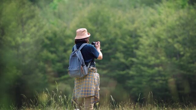 Female travel photographer taking photos with a DSLR camera while walking through a beautiful green forest, capturing nature exploration, outdoor adventure and travel photography.