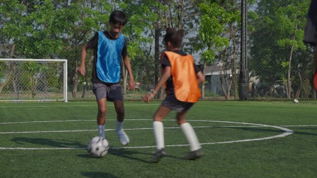 Youth soccer player dribbling ball on outdoor artificial turf during team practice, youth athlete training with teammate while opponent defends on energetic outdoor field session