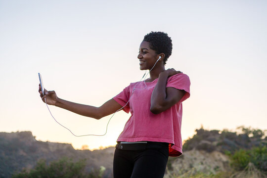 Person taking a selfie outdoors, wearing earphones and a pink shirt.