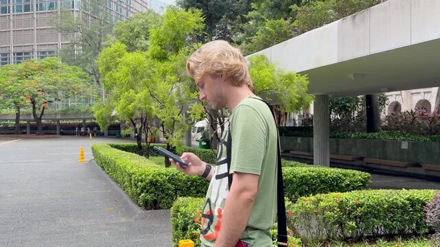 Young Man Using Smartphone Against Skyscrapers &ndash; Talking, Scrolling or Recording Video