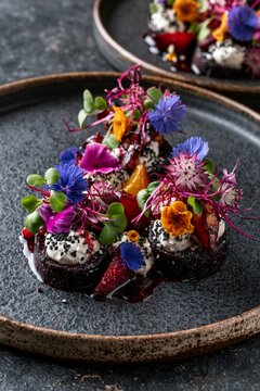 Fine dining vegan appetizer with roasted beetroot, cashew cream, microgreens, and edible flowers on dark ceramic plate, artistic gourmet presentation