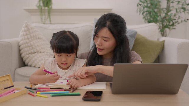 Asian mother and daughter doing homework and drawing at home beside laptop with colorful pencil, supporting family education and child learning with caring woman guidance
