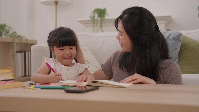 Asian mother and daughter drawing home, creative family learning activity with colorful stationery, open book, pencil practice, joyful child creativity, warm woman helping child with art table cozy