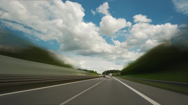Driving fast on the German Autobahn or highway on a nice sunny day with fluffy white clouds. Dynamic time lapse with motion blur.