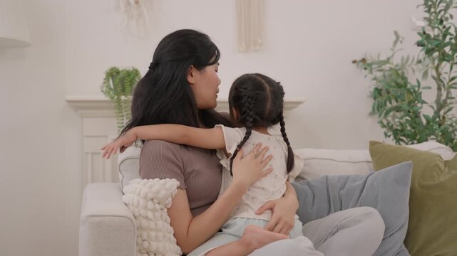 Mother embracing daughter on cozy sofa in bright living room, sharing tenderness, affection, warmth, comfort, and peaceful family connection during quiet emotional moment at home