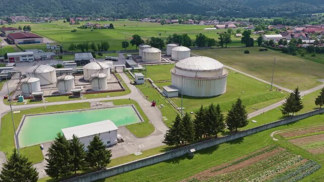 This aerial view shows a petroleum storage terminal with large fuel tanks and industrial structures near a green landscape.