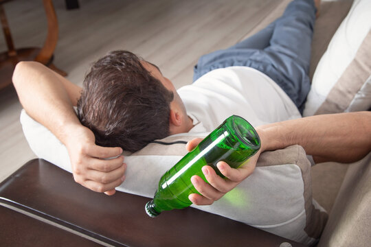 Caucasian man with a bottle of beer lying on sofa.