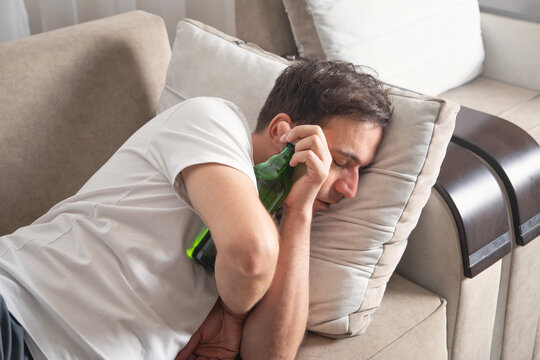Caucasian man with a bottle of beer lying on sofa.