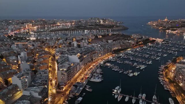 Ta' Xbiex, Malta marina with luxury yachts and boats near Manoel Island and Gzira at dusk, city lights reflecting on the Mediterranean waterfront in a drone view.