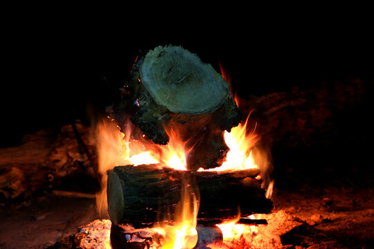 Burning logs in darkness creating a warm campfire glow with visible flames