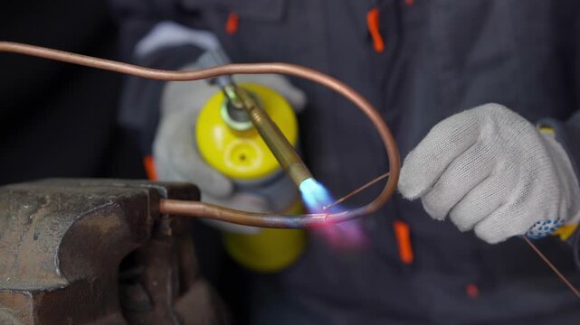 a worker brazing a copper pipe with a propane gas torch in 4K. Professional plumber soldering metal tubing with a hot blue flame, HVAC installation and repair footage