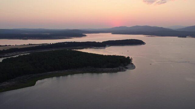 Aerial sunset over the La Cuerda del Pozo Reservoir in Spain with boats and pine forests creating a tranquil landscape