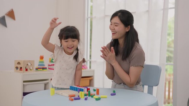 Girl and mother building colorful wooden block tower, child and family playing with toy home, smiling through creative learning activity beside bright window, sharing warm connection and focused