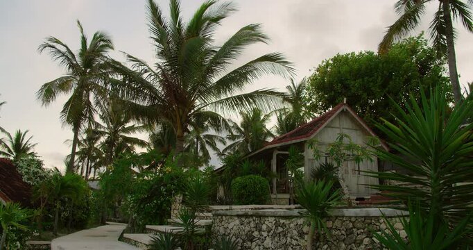 Wooden bungalow sits among palm trees and stone walls at Nusa Penida island resort