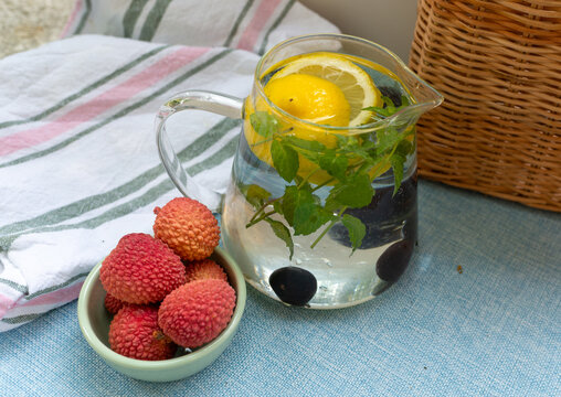 Clear infused water with whole and sliced lemon Citrus limon and fresh mint Mentha leaves served in a glass pitcher beside ripe lychee fruit Litchi chinensis. Refreshing summer drink concept for hydra