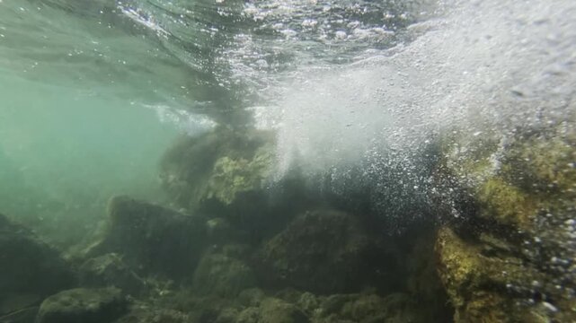 Undersea view of green ocean water, light creating patterns on the surface, and ancient rocks covered in algae and marine growth