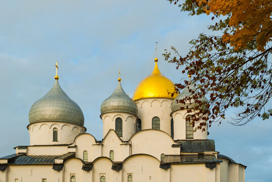 St Sophia cathedral in Veliky Novgorod Russia. Autumn cathedral architecture with golden and silver domes under a cloudy sky, framed by colorful tree branches