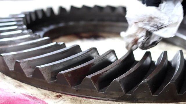 Wiping down a large industrial gear with a cloth during inspection.