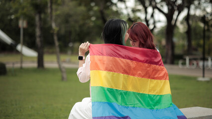 Naklejka premium Intimate Lesbian Couple Sharing Moment Covered in LGBT Rainbow Flag in Park