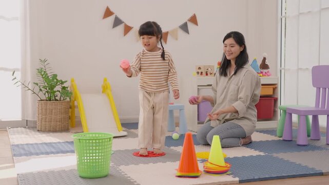 Mother and child playing colorful block, cone, ball, basket, and toy slide game in bright playroom, enjoying cheerful family learning activity with joyful movement indoors beside soft floor mat