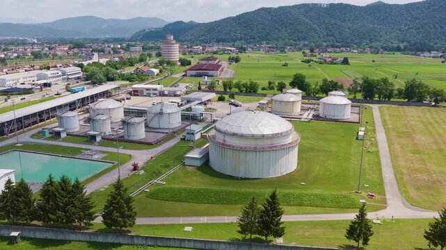 Large industrial oil storage tanks are seen at a petroleum depot with green fields nearby. The view shows energy infrastructure in the area.