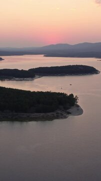 Drone flying over La Cuerda del Pozo Reservoir in Soria with a pink sunset reflecting on the calm water
