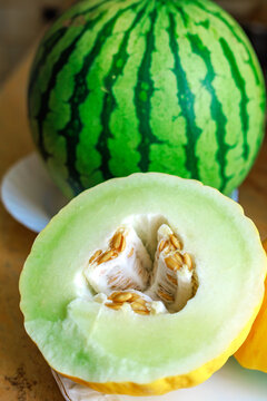 Cut ripe melon showing pale green flesh and seeds with a small striped watermelon in the background. Concept of fresh summer fruit, melon varieties and healthy seasonal food.