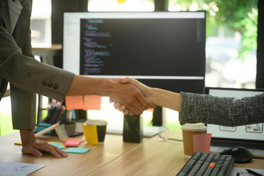 Close up of Business Handshake at Tech Office Desk with Code on Monitor Screen