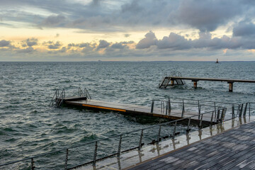 Fototapeta premium Pier with stairs leading into the choppy sea and a distant lighthouse. Malmo