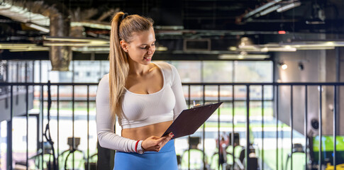 Fototapeta premium Female personal fitness coach examining training schedule on clipboard indoors.