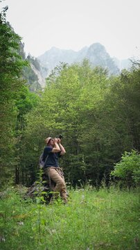 Female hiker taking photos with a professional camera while exploring a scenic forest with mountain views, combining hiking, travel and nature photography.