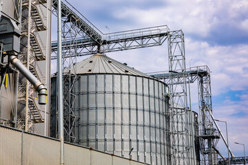 Large metallic grain silos and industrial structures under a cloudy sky, ideal for illustrating agriculture, storage, and food production concepts. © Alexandra
