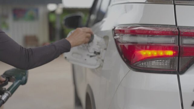 person's hand holding a green fuel pump nozzle, refilling a white car with diesel at a gas station. Concept of automotive transportation, energy cost, and daily driving commute.